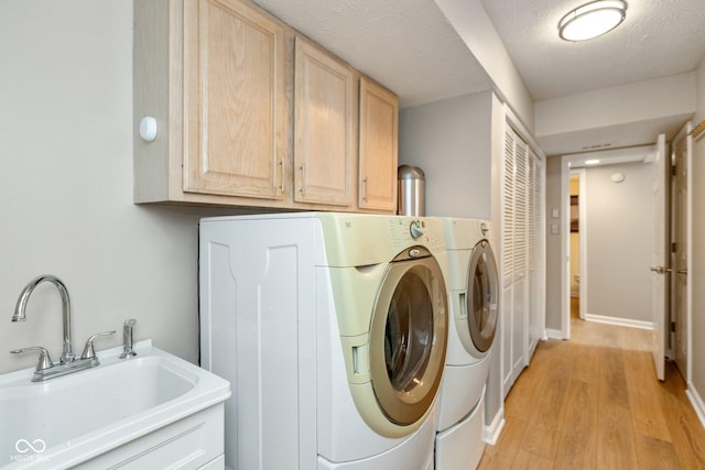 laundry room with a textured ceiling, washer and clothes dryer, light wood-type flooring, cabinets, and sink