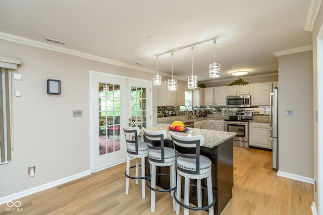 kitchen with appliances with stainless steel finishes, track lighting, ornamental molding, pendant lighting, and decorative backsplash