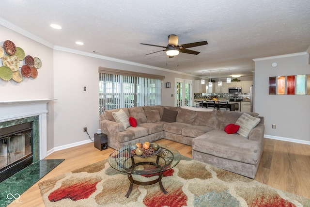 living room featuring a textured ceiling, hardwood / wood-style floors, crown molding, a fireplace, and ceiling fan