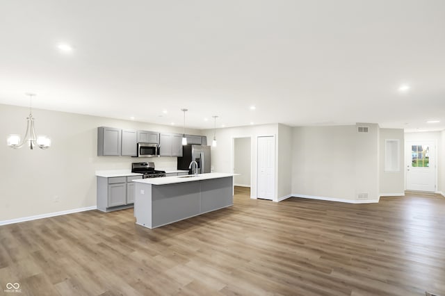 kitchen with sink, an inviting chandelier, an island with sink, gray cabinetry, and stainless steel appliances