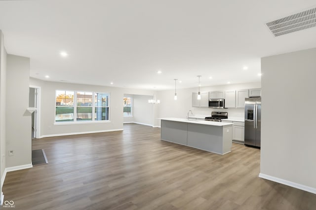 kitchen featuring pendant lighting, a center island with sink, an inviting chandelier, light wood-type flooring, and stainless steel appliances