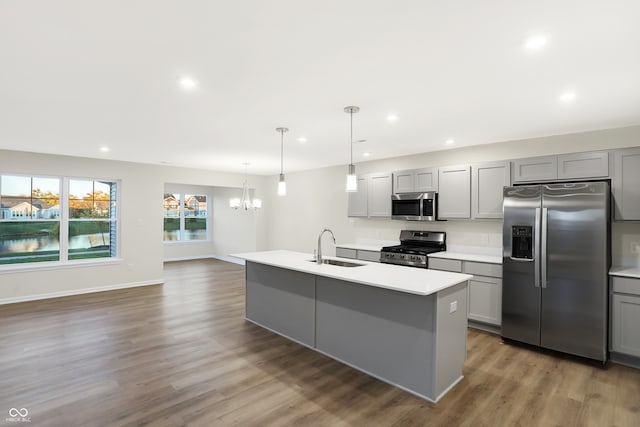 kitchen with appliances with stainless steel finishes, an island with sink, hanging light fixtures, gray cabinets, and a chandelier