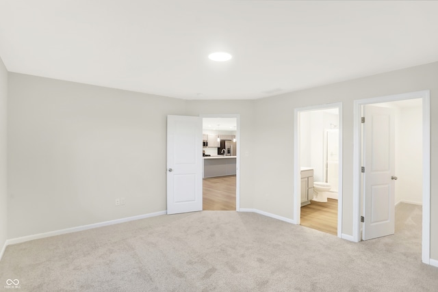 unfurnished bedroom with ensuite bathroom, light colored carpet, and stainless steel fridge