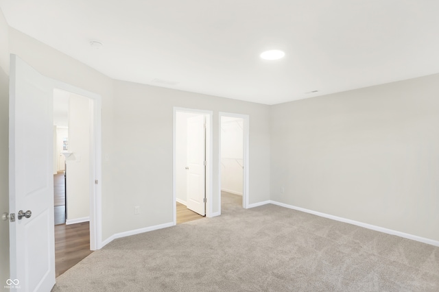 unfurnished bedroom with a spacious closet, a closet, connected bathroom, and light colored carpet