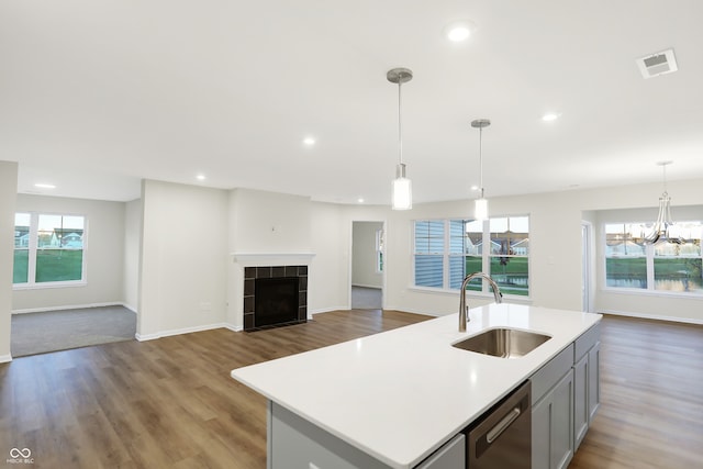 kitchen with an island with sink, decorative light fixtures, a fireplace, stainless steel dishwasher, and sink