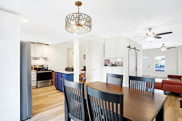 dining room with a barn door, ceiling fan with notable chandelier, and light wood-type flooring