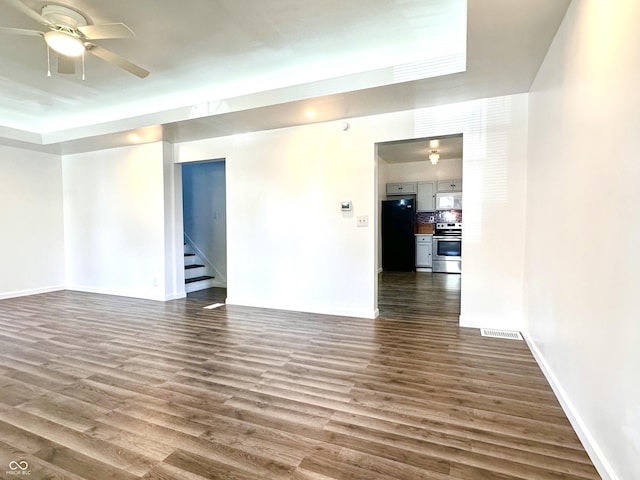 spare room featuring dark wood-style floors, visible vents, stairway, and a ceiling fan