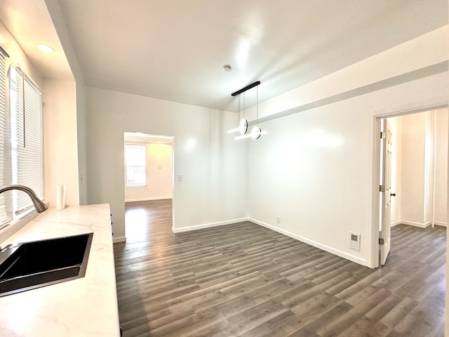 unfurnished dining area featuring dark wood-type flooring, a sink, visible vents, and baseboards