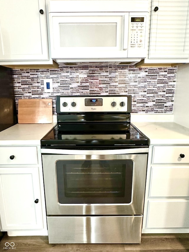 kitchen featuring white microwave, tasteful backsplash, stainless steel electric range, and white cabinets