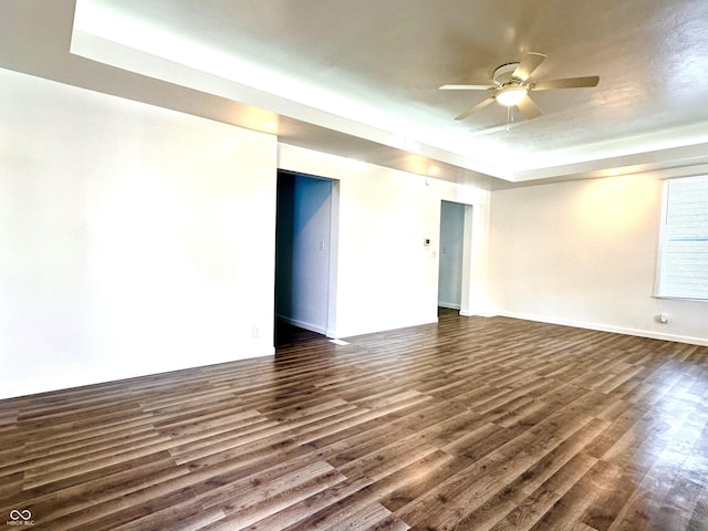 spare room featuring dark wood-style floors, ceiling fan, a raised ceiling, and baseboards