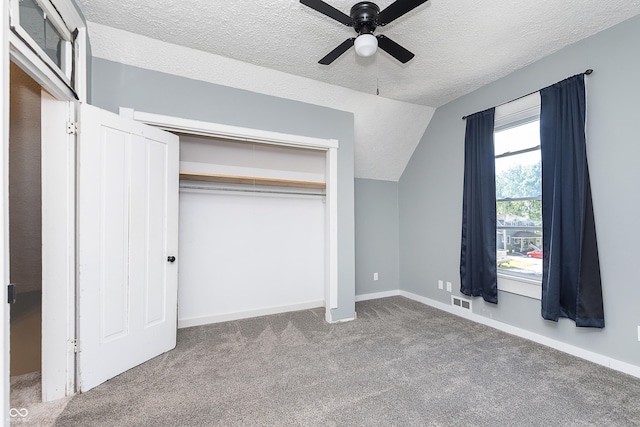 unfurnished bedroom with lofted ceiling, a textured ceiling, a closet, ceiling fan, and carpet