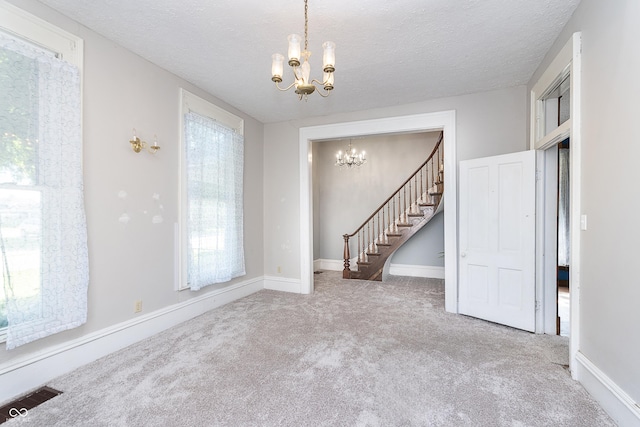 carpeted empty room with a healthy amount of sunlight, a textured ceiling, and a chandelier