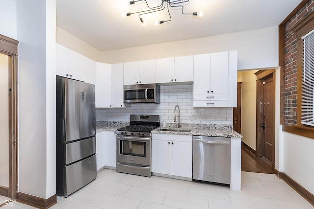 kitchen with appliances with stainless steel finishes, tasteful backsplash, light stone counters, sink, and white cabinetry