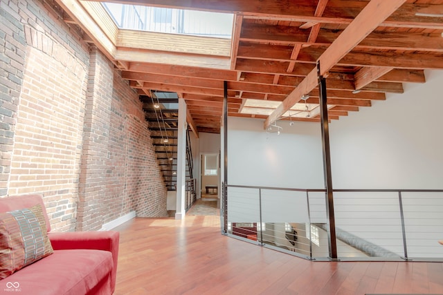 sitting room with beam ceiling, a towering ceiling, brick wall, and hardwood / wood-style flooring