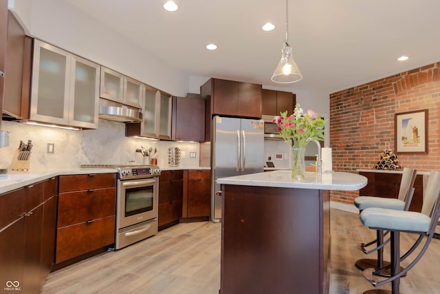 kitchen with hanging light fixtures, brick wall, backsplash, light hardwood / wood-style floors, and appliances with stainless steel finishes