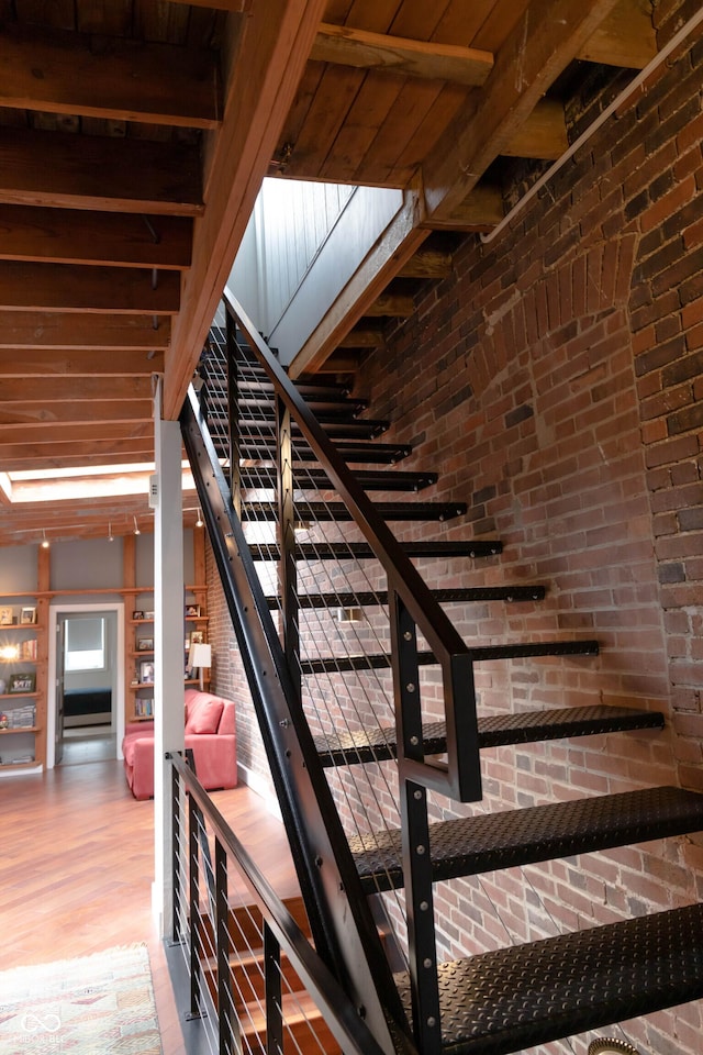 stairs featuring beamed ceiling and brick wall