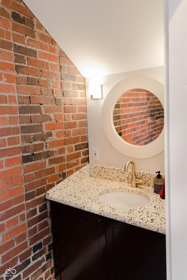 bathroom featuring vanity, lofted ceiling, and brick wall