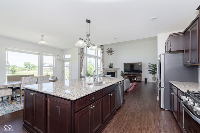 kitchen with appliances with stainless steel finishes, dark wood-type flooring, sink, pendant lighting, and a center island with sink