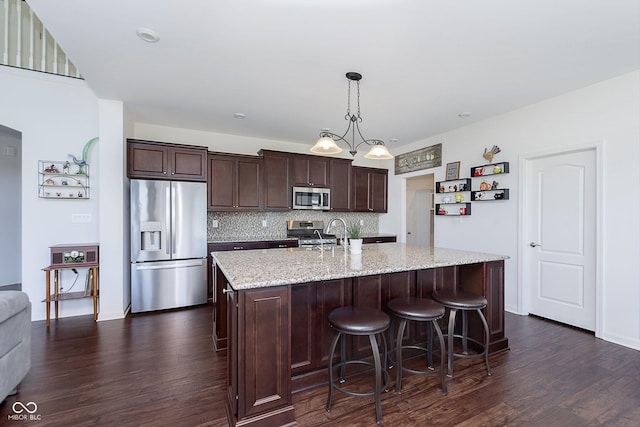 kitchen with a kitchen island with sink, hanging light fixtures, decorative backsplash, appliances with stainless steel finishes, and dark brown cabinets