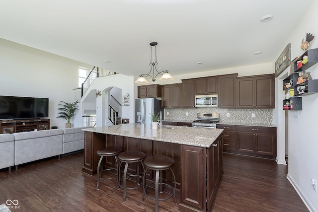 kitchen with decorative backsplash, appliances with stainless steel finishes, dark brown cabinetry, hanging light fixtures, and an island with sink