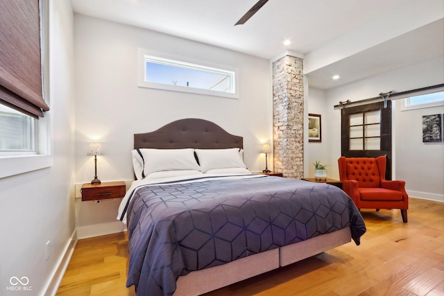 bedroom featuring a barn door, ceiling fan, and light hardwood / wood-style floors