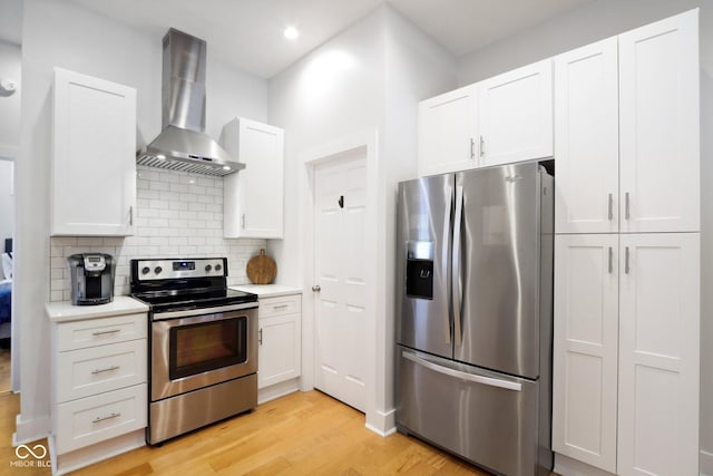 kitchen featuring white cabinets, light hardwood / wood-style flooring, wall chimney exhaust hood, tasteful backsplash, and stainless steel appliances