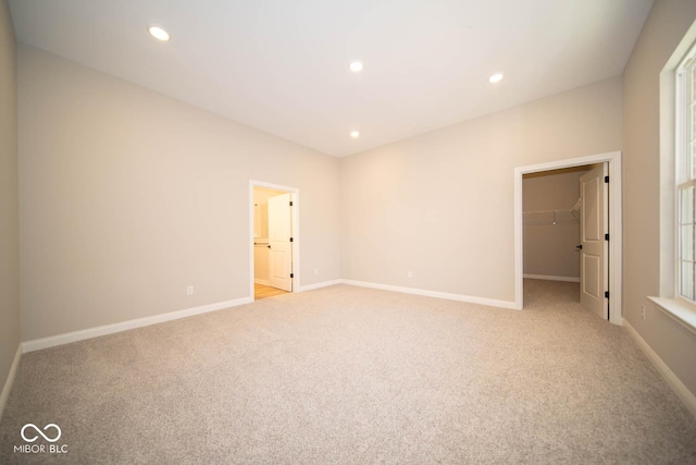 unfurnished bedroom featuring ensuite bath, a walk in closet, light carpet, and a closet