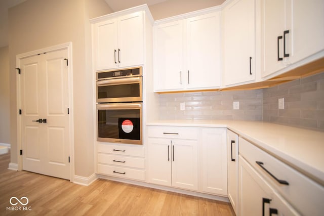 7936 Beaumont Green Pl, Indianapolis, IN 46250 - kitchen featuring stainless steel double oven, white cabinetry, light wood-style flooring, light countertops, and backsplash