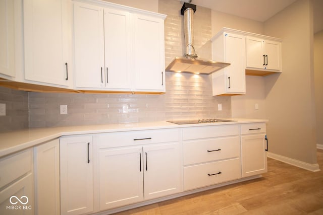 kitchen with white cabinets, black electric cooktop, wall chimney exhaust hood, and light hardwood / wood-style floors