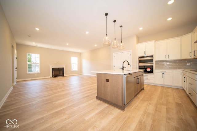 kitchen featuring a kitchen island with sink, white cabinets, sink, hanging light fixtures, and stainless steel appliances