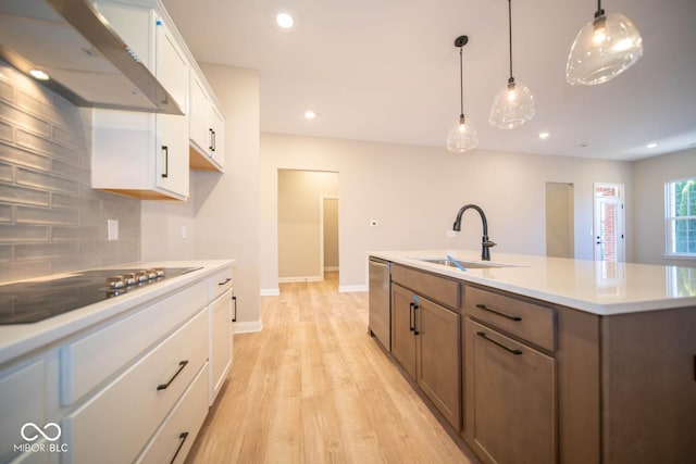 kitchen with a kitchen island with sink, wall chimney range hood, sink, stainless steel dishwasher, and white cabinetry