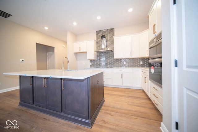 kitchen featuring white cabinets, sink, a kitchen island with sink, and tasteful backsplash