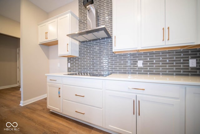 kitchen featuring decorative backsplash, black cooktop, wall chimney range hood, wood-type flooring, and white cabinets