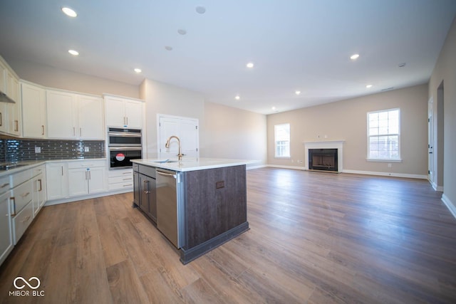 kitchen with sink, light wood-type flooring, a center island with sink, white cabinets, and appliances with stainless steel finishes