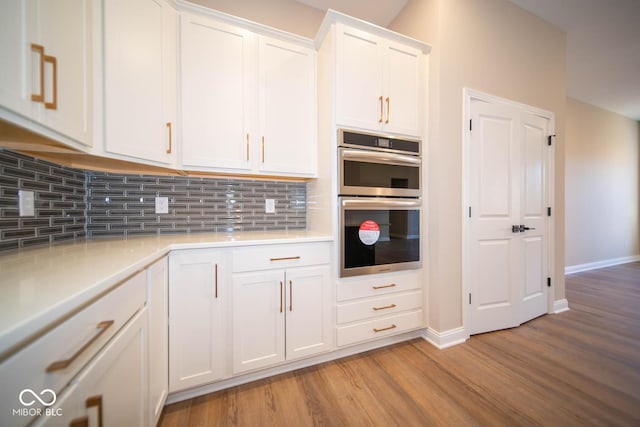 kitchen with white cabinets, decorative backsplash, light wood-type flooring, and double oven