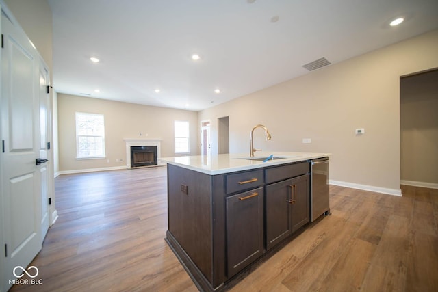 kitchen featuring dishwasher, sink, light hardwood / wood-style floors, dark brown cabinets, and a center island with sink