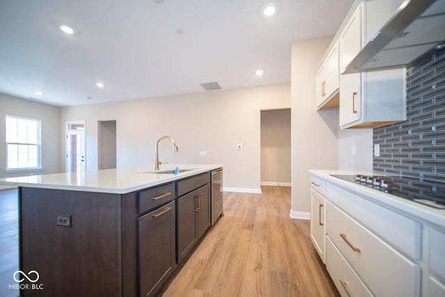 kitchen featuring wall chimney exhaust hood, sink, white cabinetry, and a kitchen island with sink