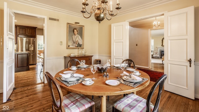 dining area with dark wood-type flooring, ornamental molding, and a notable chandelier