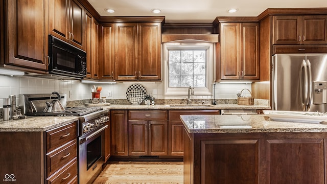 kitchen featuring sink, backsplash, stainless steel appliances, light stone counters, and light wood-type flooring