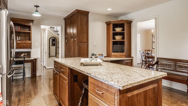 kitchen with a kitchen island, dark hardwood / wood-style floors, stainless steel refrigerator, hanging light fixtures, and light stone countertops