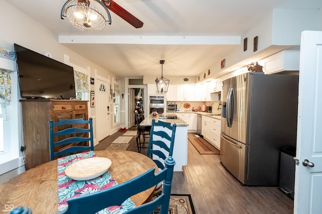 kitchen featuring white cabinets, hanging light fixtures, a kitchen island with sink, and appliances with stainless steel finishes