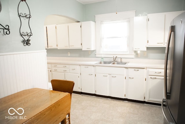 kitchen with stainless steel refrigerator, sink, white cabinets, and decorative light fixtures