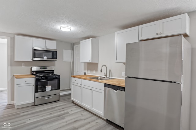 kitchen with wooden counters, appliances with stainless steel finishes, sink, and white cabinetry