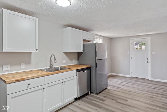 kitchen featuring light hardwood / wood-style flooring, butcher block counters, sink, white cabinets, and appliances with stainless steel finishes