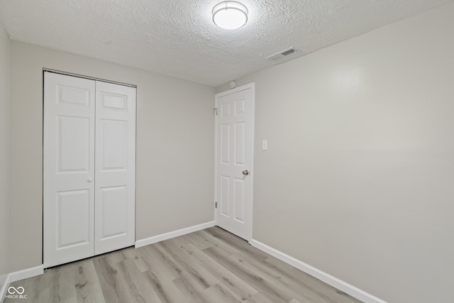 unfurnished bedroom featuring a closet, light hardwood / wood-style flooring, and a textured ceiling