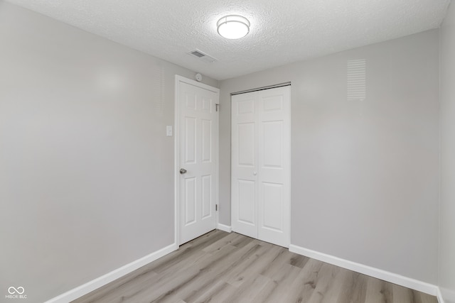 unfurnished bedroom with a closet, light hardwood / wood-style flooring, and a textured ceiling