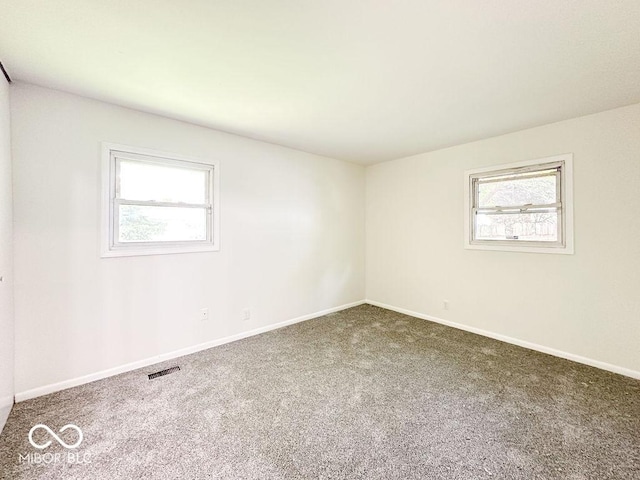 carpeted spare room featuring baseboards, visible vents, and a wealth of natural light