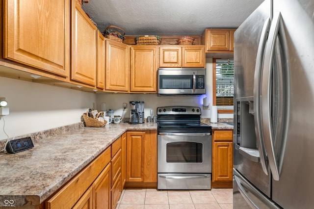 kitchen with light tile patterned floors, light stone countertops, a textured ceiling, and appliances with stainless steel finishes