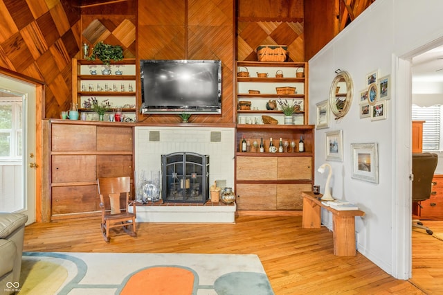 living room featuring wooden walls, a fireplace, lofted ceiling, light hardwood / wood-style floors, and built in shelves