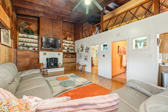 living room featuring wood ceiling, beam ceiling, a brick fireplace, built in shelves, and light wood-type flooring